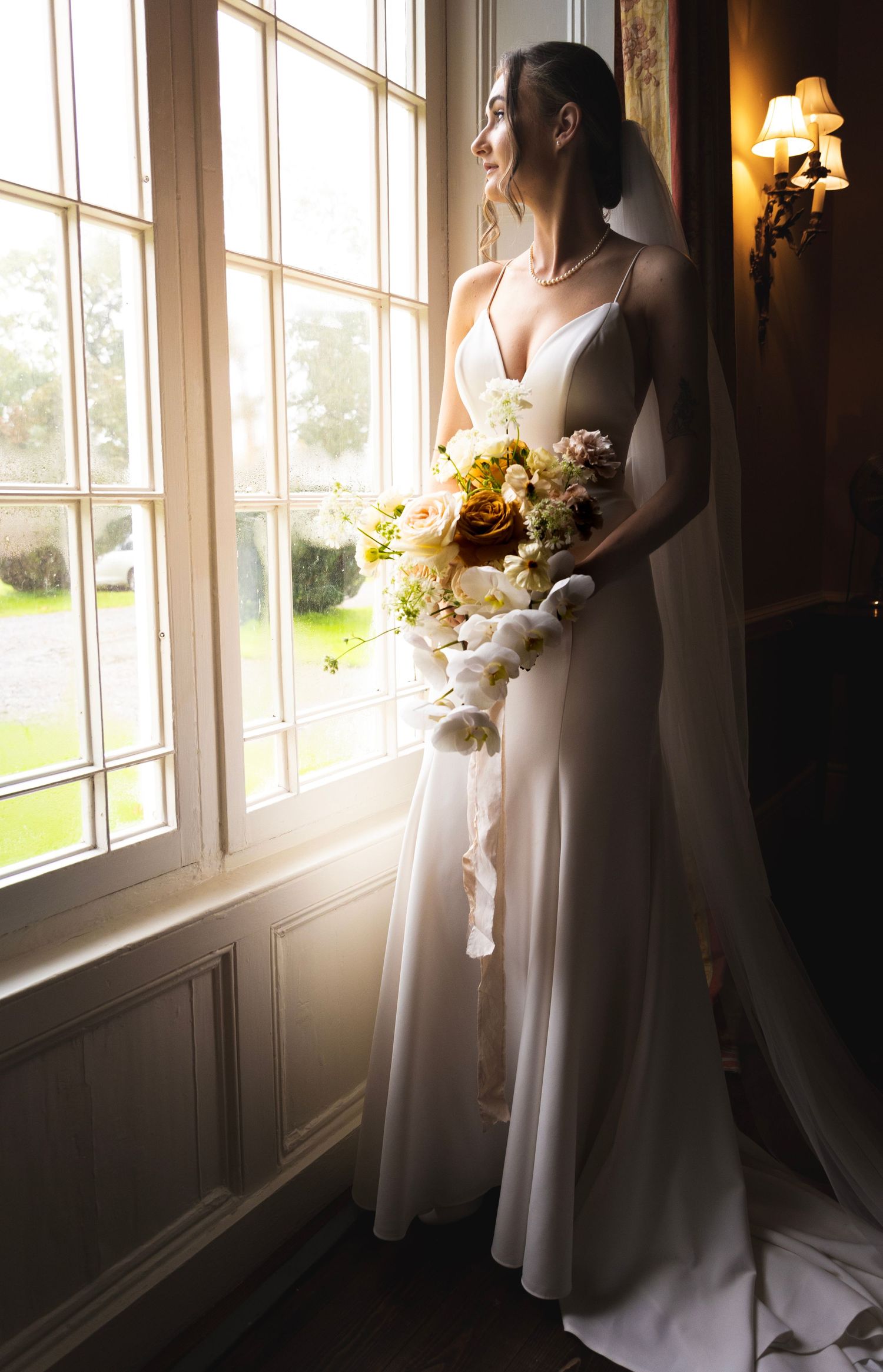 A sunlit bridal portrait by a window with a beautiful bouquet of yellow and white flowers.