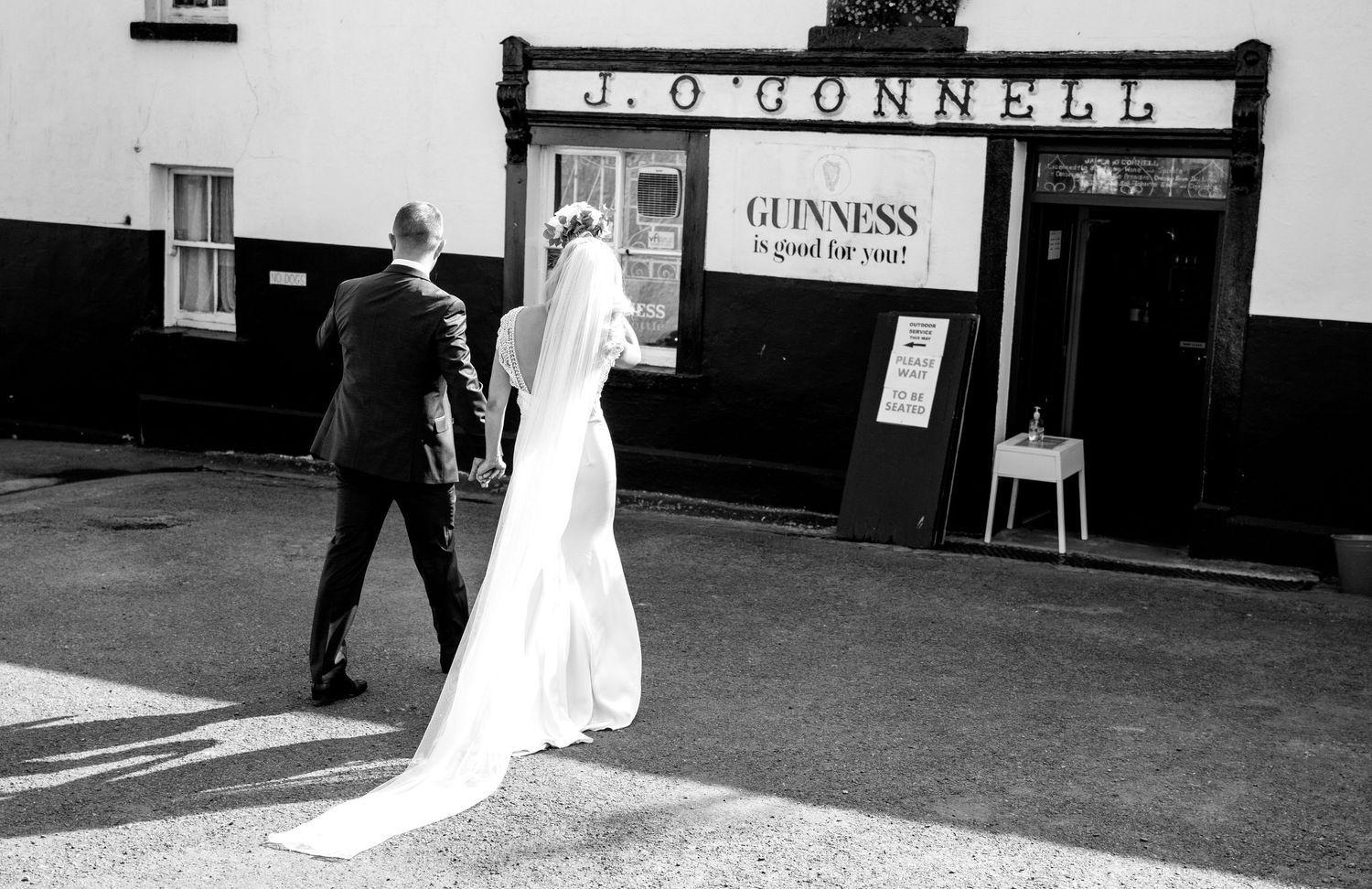 Black and white photo of couple walking towards traditional Irish pub on their wedding day.