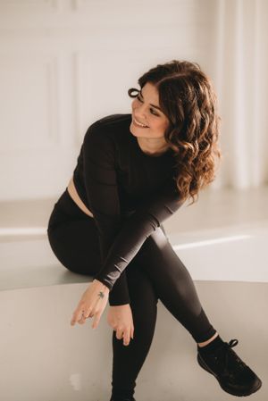 Casual studio pose in all-black athletic wear with curled hair against white backdrop.