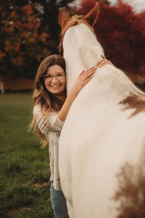 Joyful moment with a white horse against vibrant fall foliage background.