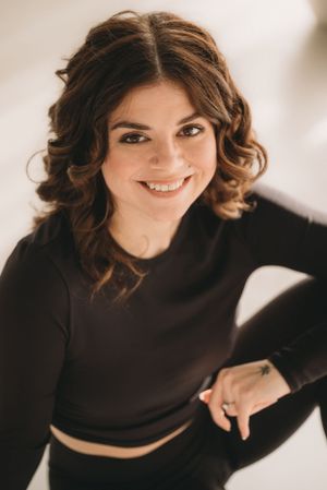 Studio portrait featuring wavy hair, natural makeup, and a black long-sleeve crop top.