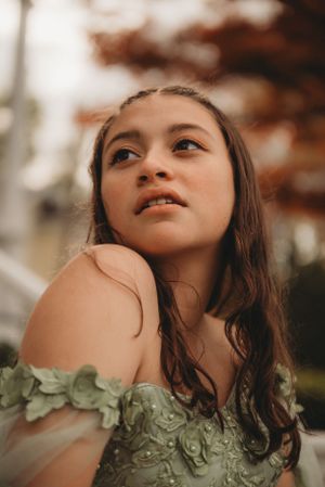 Artistic portrait of someone wearing an elegant sage green dress with off-shoulder design in warm sunlight.