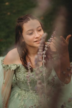 A dreamy portrait in a sage green dress with delicate floral details and sheer sleeves against a natural outdoor backdrop.