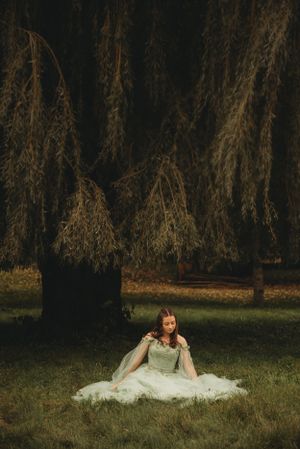 Ethereal bridal portrait under weeping willow trees creates dramatic outdoor scene.