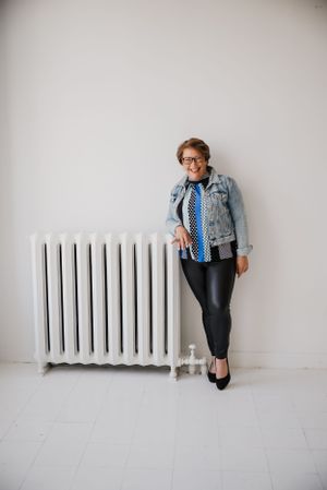 Stylish casual look with denim jacket, polka dot top, and black pants next to vintage radiator.