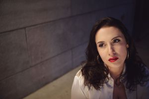 Portrait of person in white shirt against dark wall with dramatic lighting.