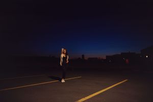 Silhouette of person standing on dark road with glowing horizon.