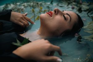 Artistic portrait of person in water surrounded by floating leaves.