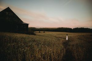 Moody sunset landscape with silhouette of barn and figure standing in field.
