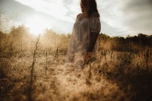 Dreamy silhouette of person standing in golden sunlit field at dusk.