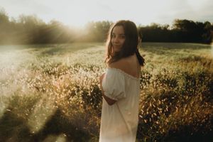 Person in white dress standing in sunlit meadow during golden hour.