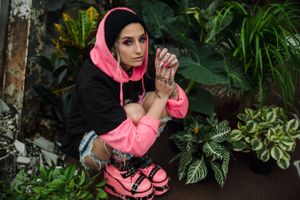 Someone in a pink hoodie poses among lush tropical plants and greenery.