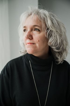 Portrait of person with silver hair wearing black turtleneck against white background.