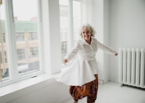 Someone twirling in a white dress and patterned pants in a bright white room with windows.