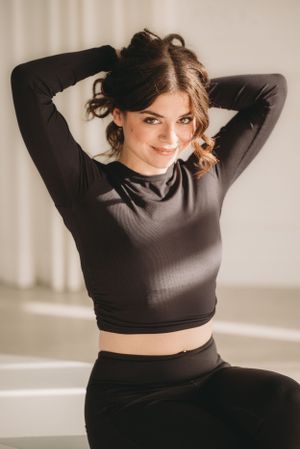 Athletic pose in a black crop top and leggings against a white studio background.