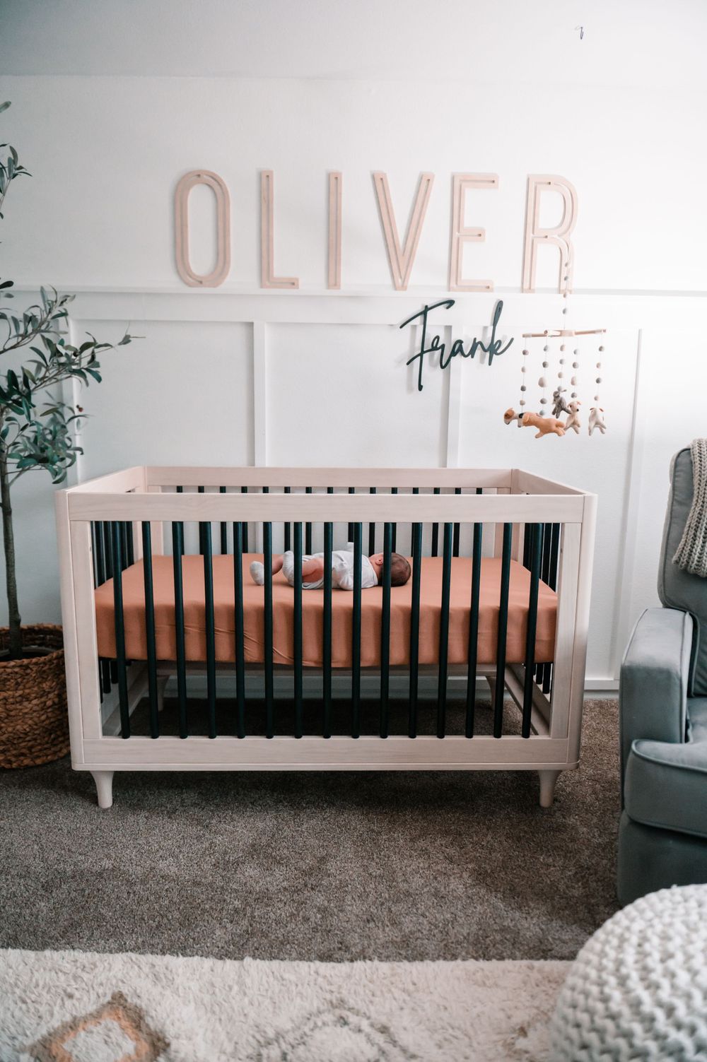 Modern white nursery with Oliver name sign and black crib against gray walls.