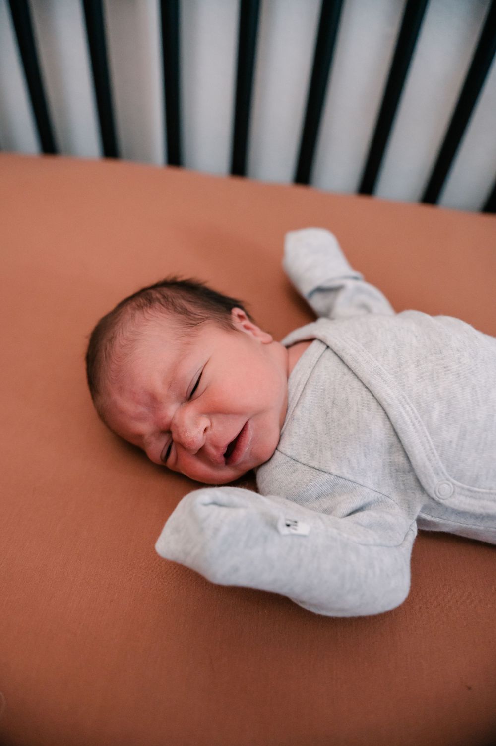 Newborn baby sleeping peacefully in gray onesie on orange bedding.