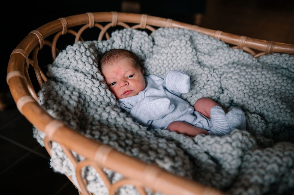 Baby nestled in woven basket with thick knitted gray blanket.