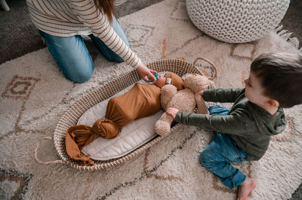 Newborn photography session showing a baby wrapped in a brown swaddle on a textured cream rug.