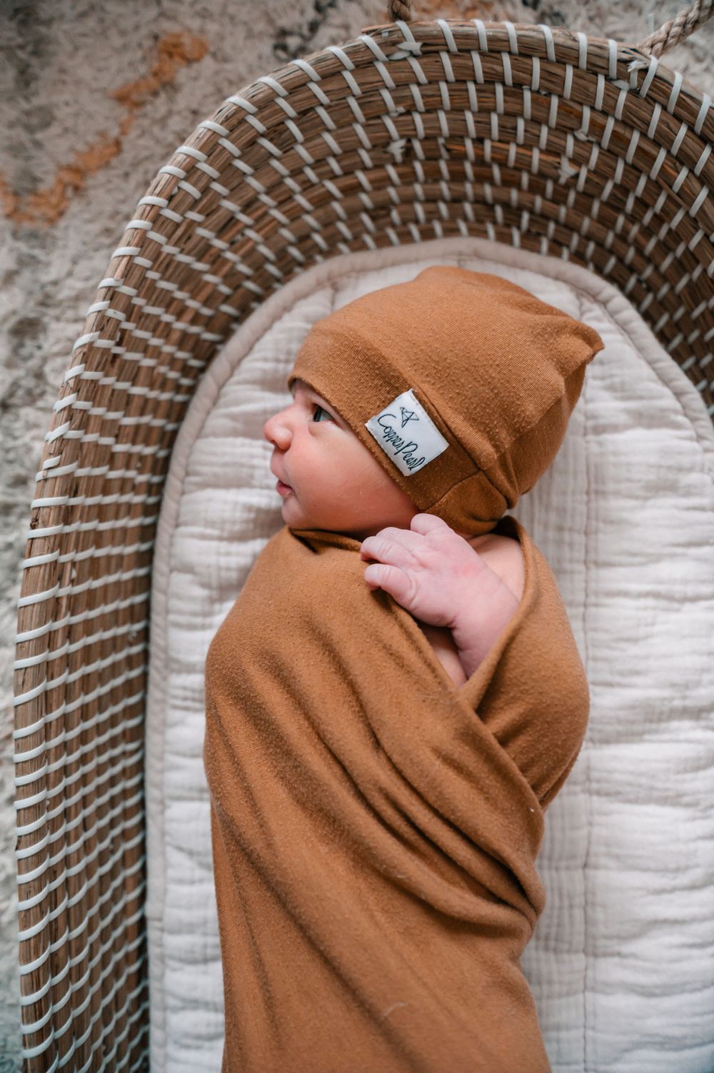 Baby swaddled in caramel-colored blanket resting on a woven basket bed.