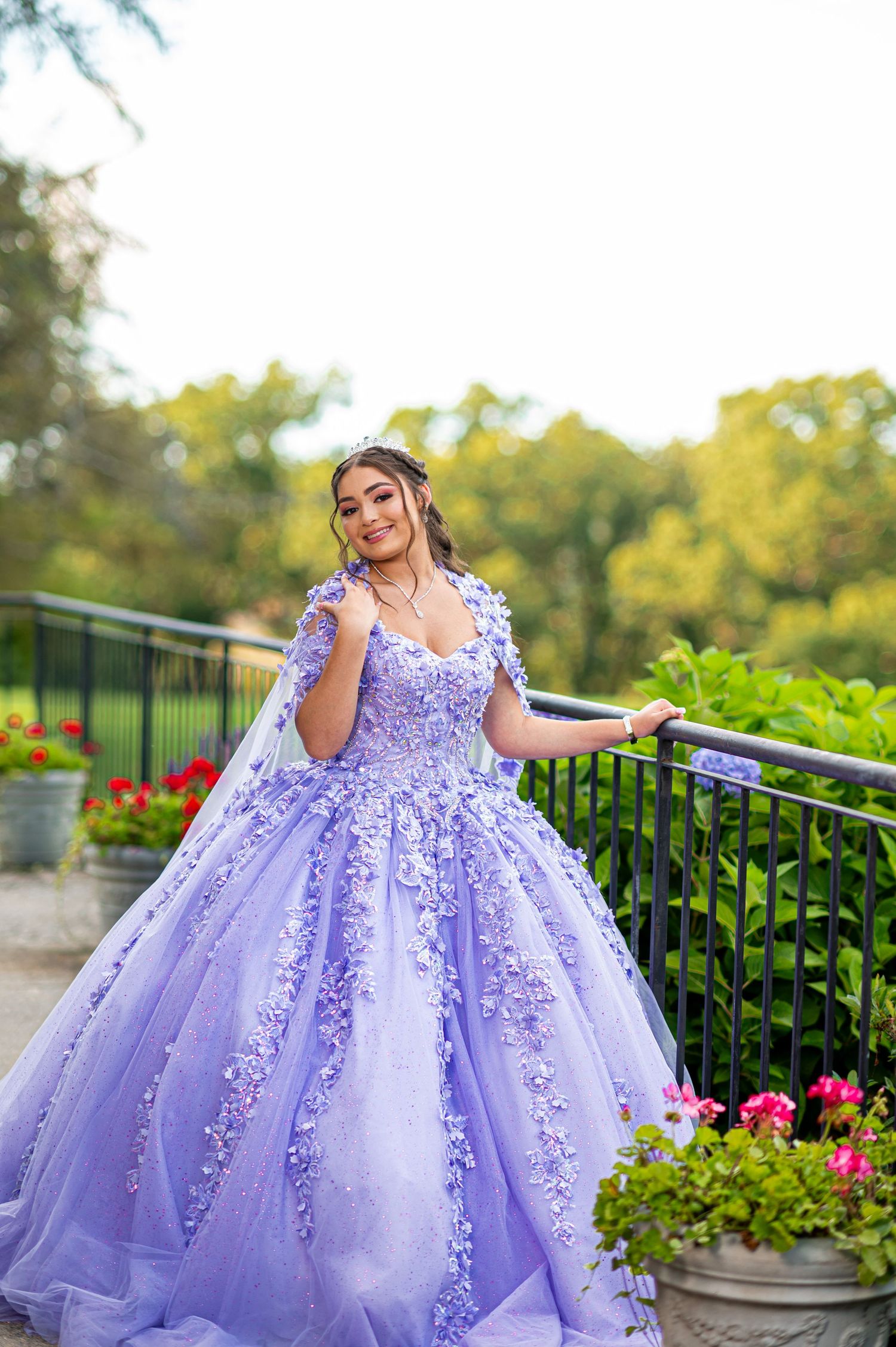 A lavender princess ball gown with floral appliques photographed in a garden setting.