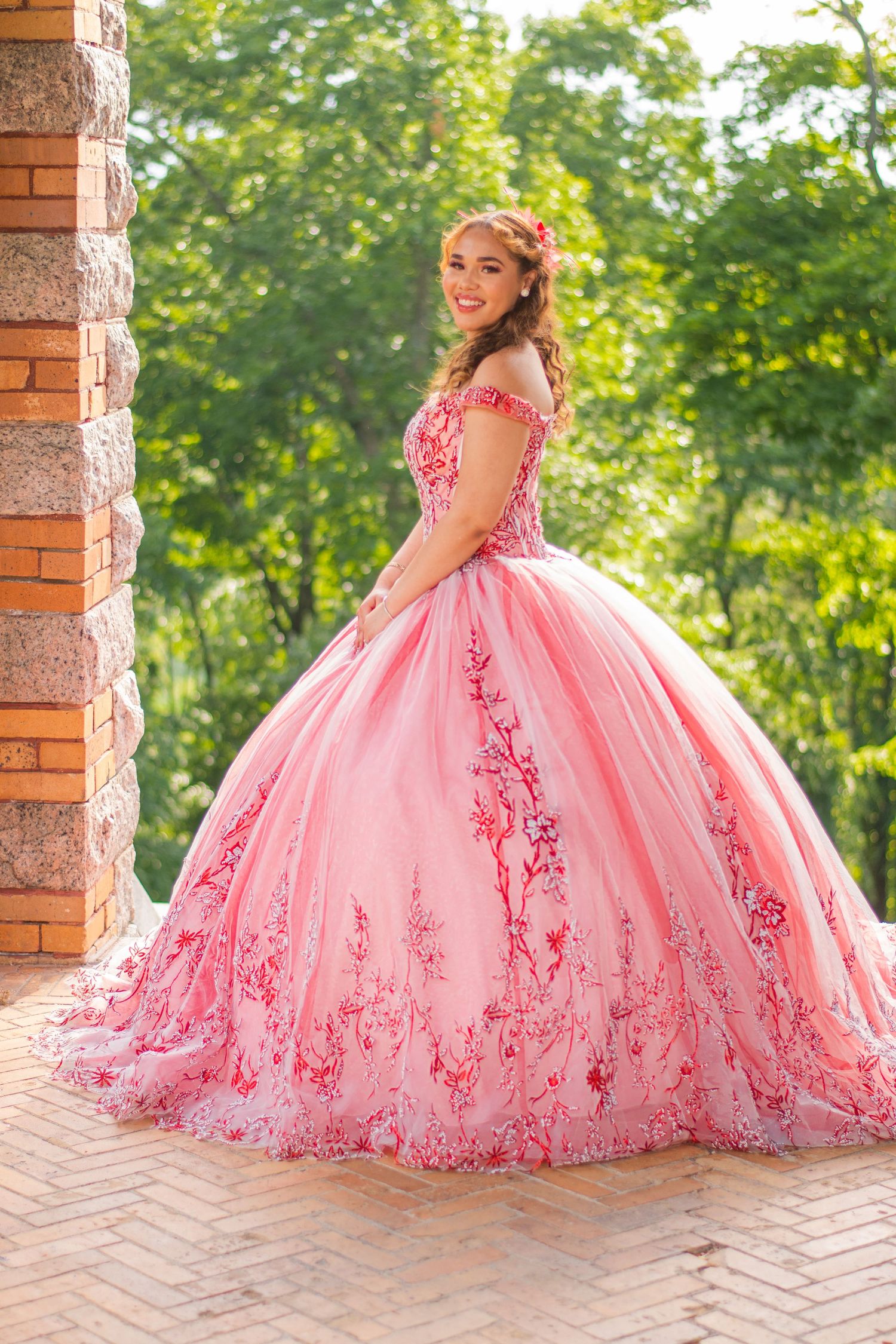 A stunning pink ballgown with intricate floral embroidery photographed against a lush garden backdrop.