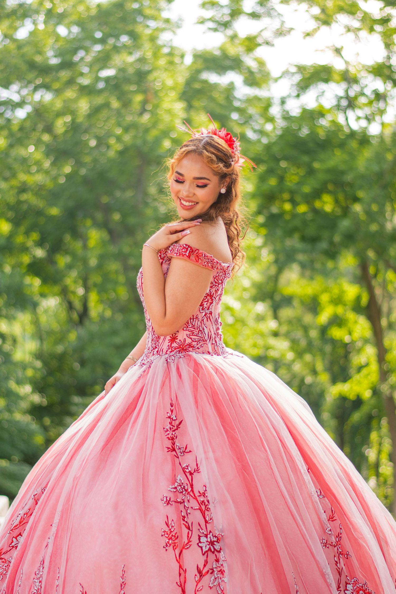 An elegant pink quinceañera dress with detailed embellishments shown in an outdoor garden setting.