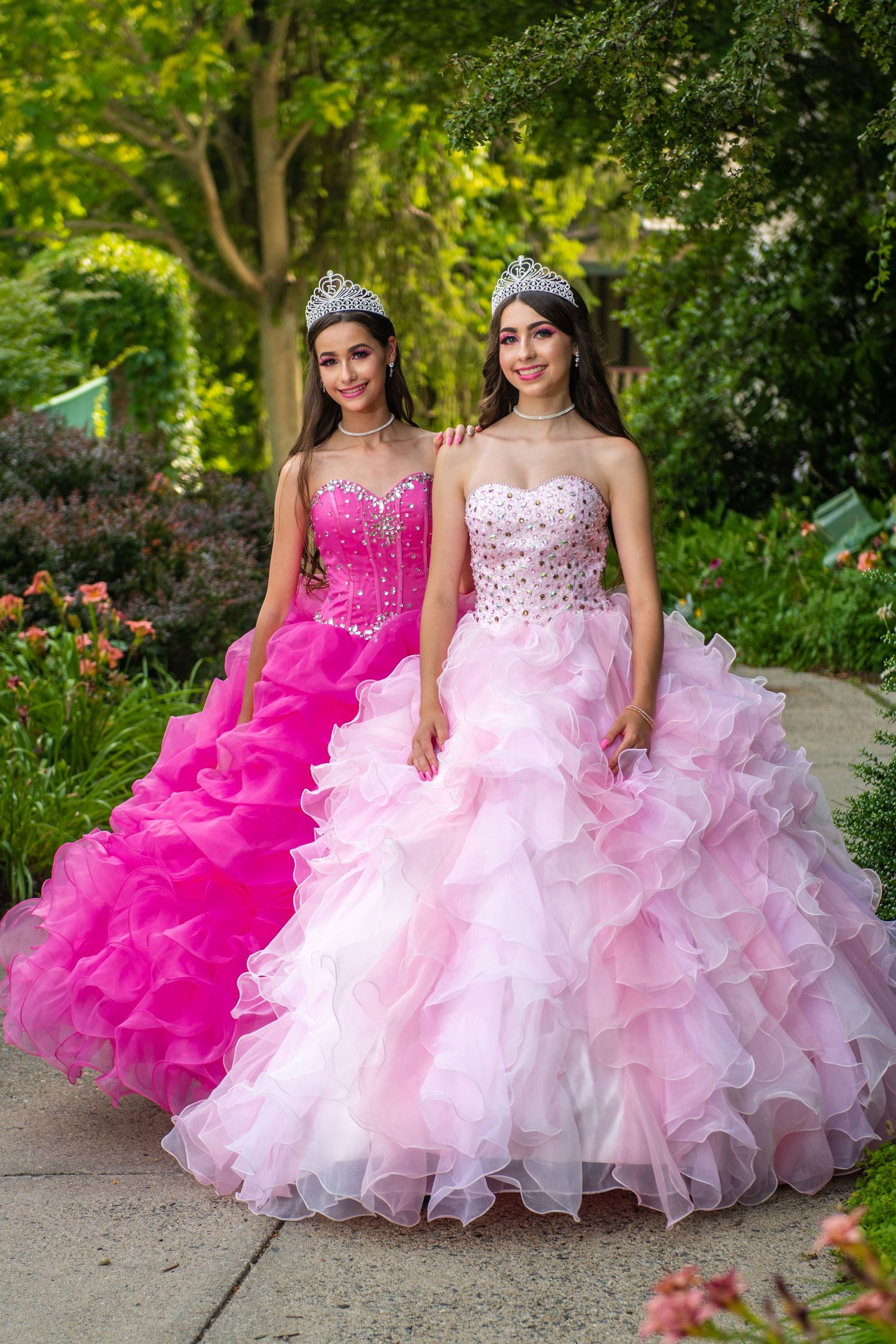 Two quinceañera dresses in hot pink and light pink photographed in a lush garden setting.