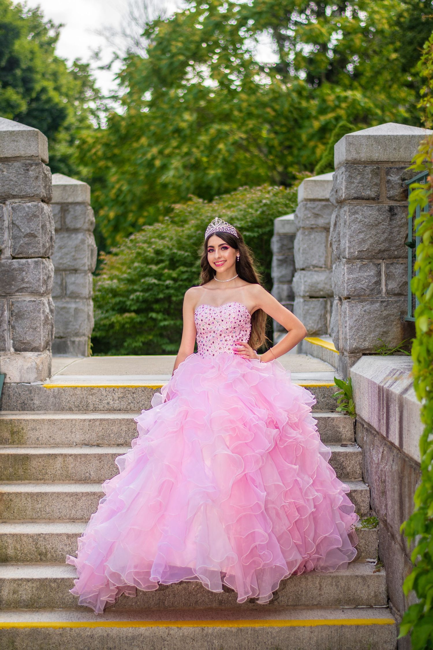 Princess-style pink ball gown photographed on stone steps in an elegant garden setting.
