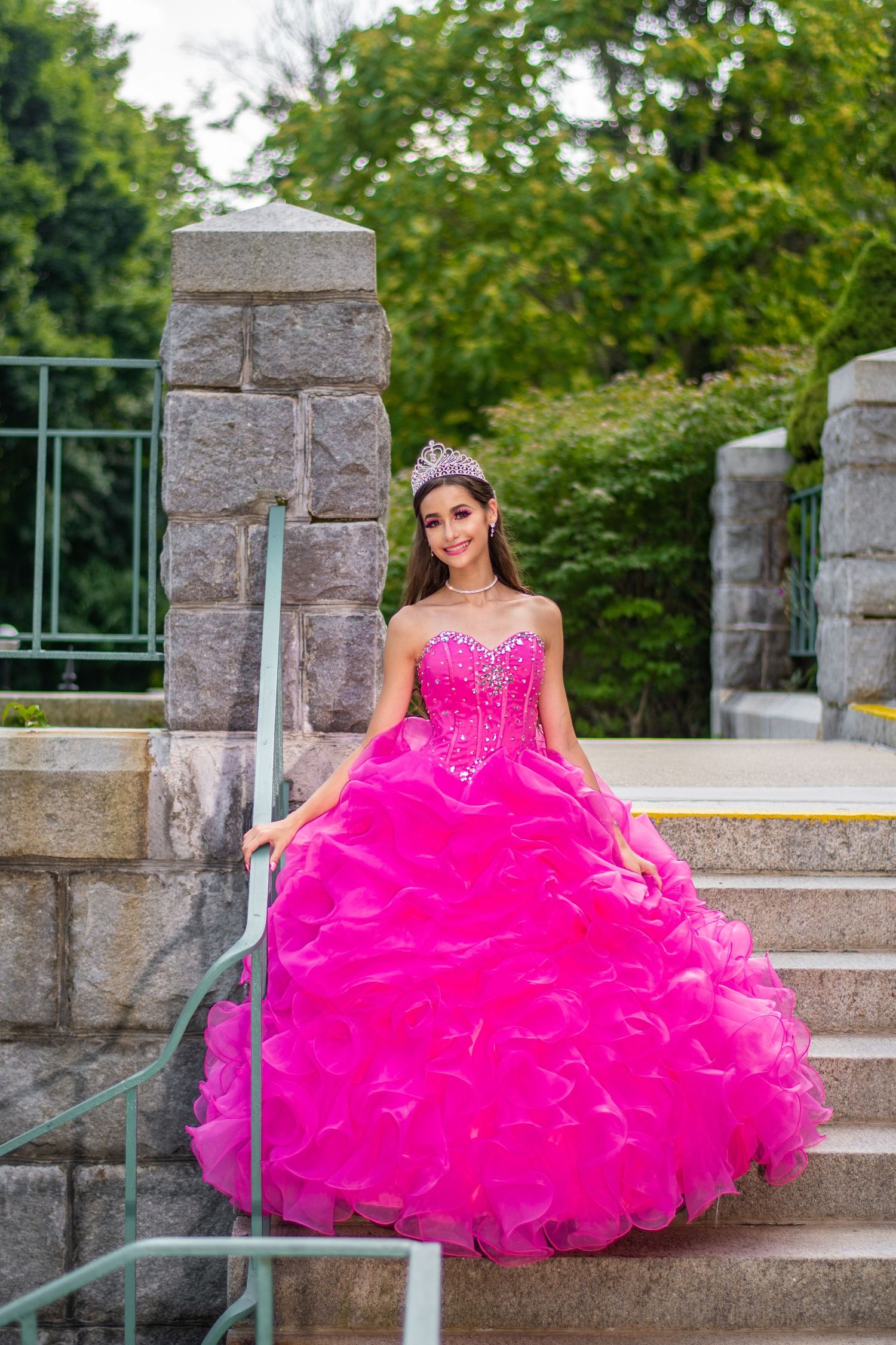 Vibrant hot pink quinceañera dress photographed on stone steps outdoors.