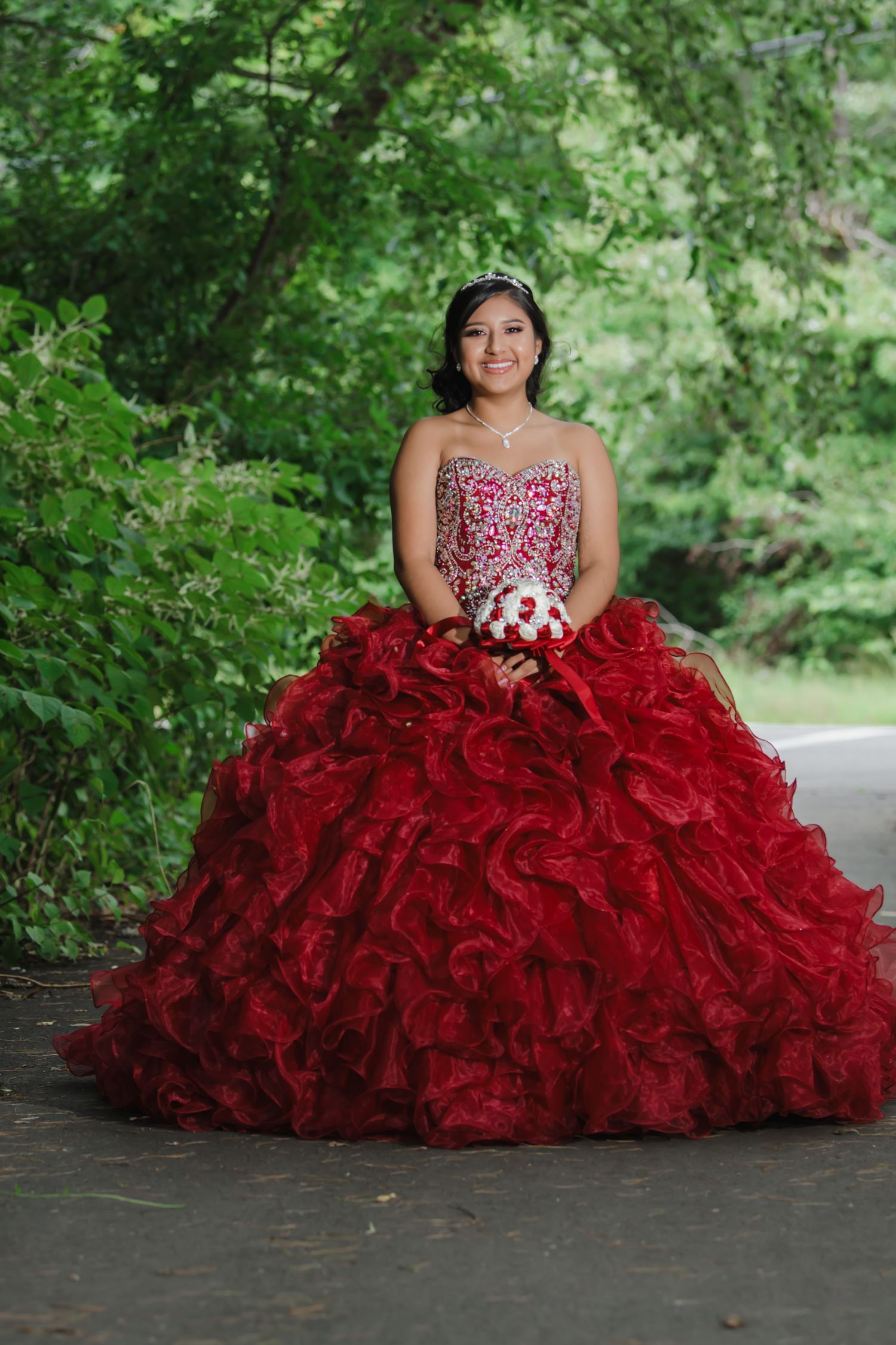 A dramatic red ruffled ball gown photographed in a lush green garden setting.