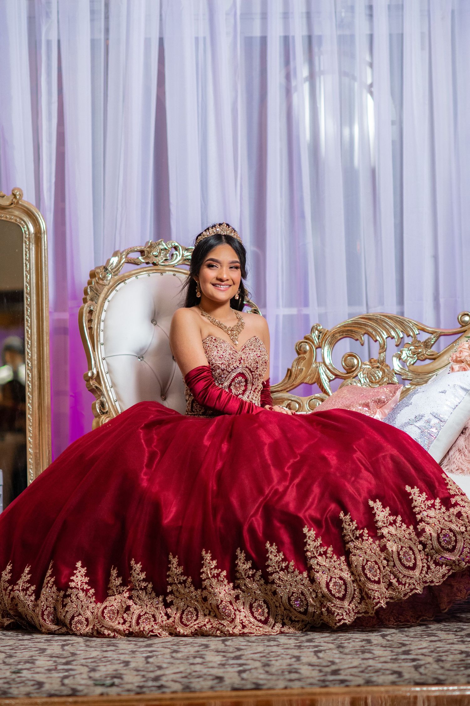 Red ball gown with gold embroidery showcased on elegant white tufted settee.