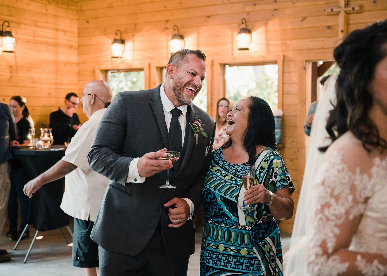 Joyful celebration at a wedding reception in a rustic wooden venue with guests dancing and laughing.