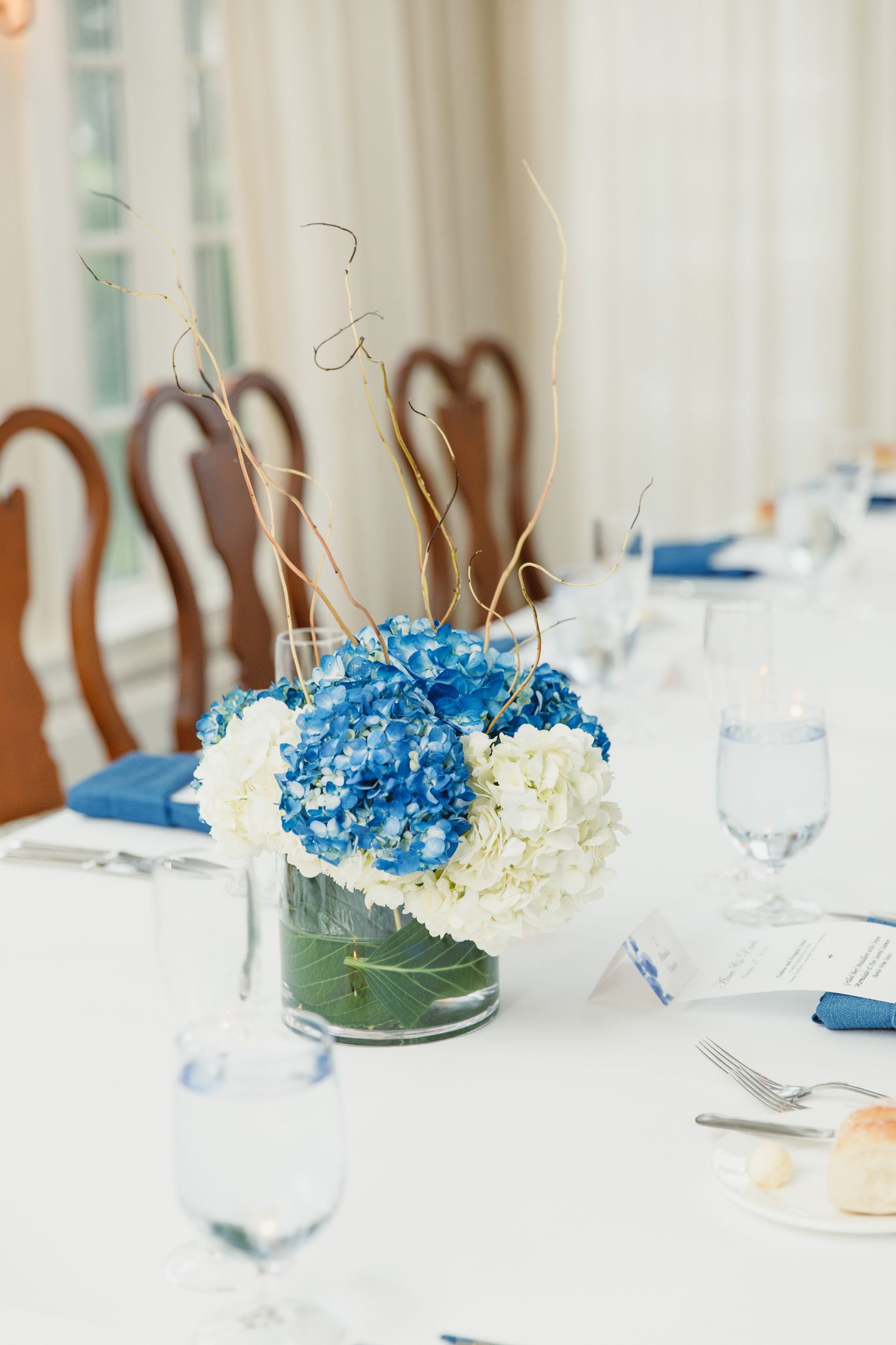 Elegant table setting with blue hydrangea centerpieces and white linens at a wedding reception.