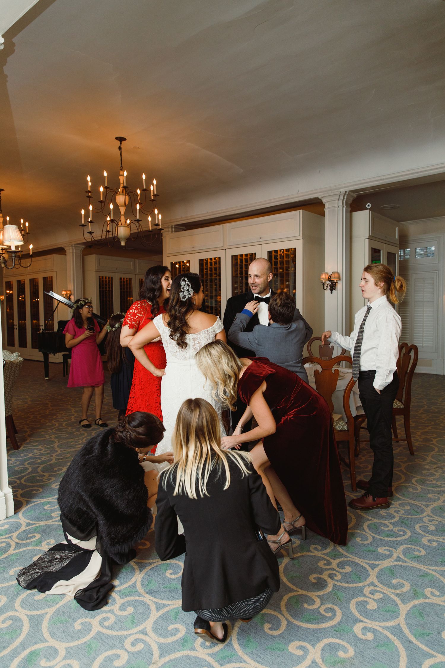 Wedding guests gathered in a reception hall with chandelier lighting and patterned carpet.