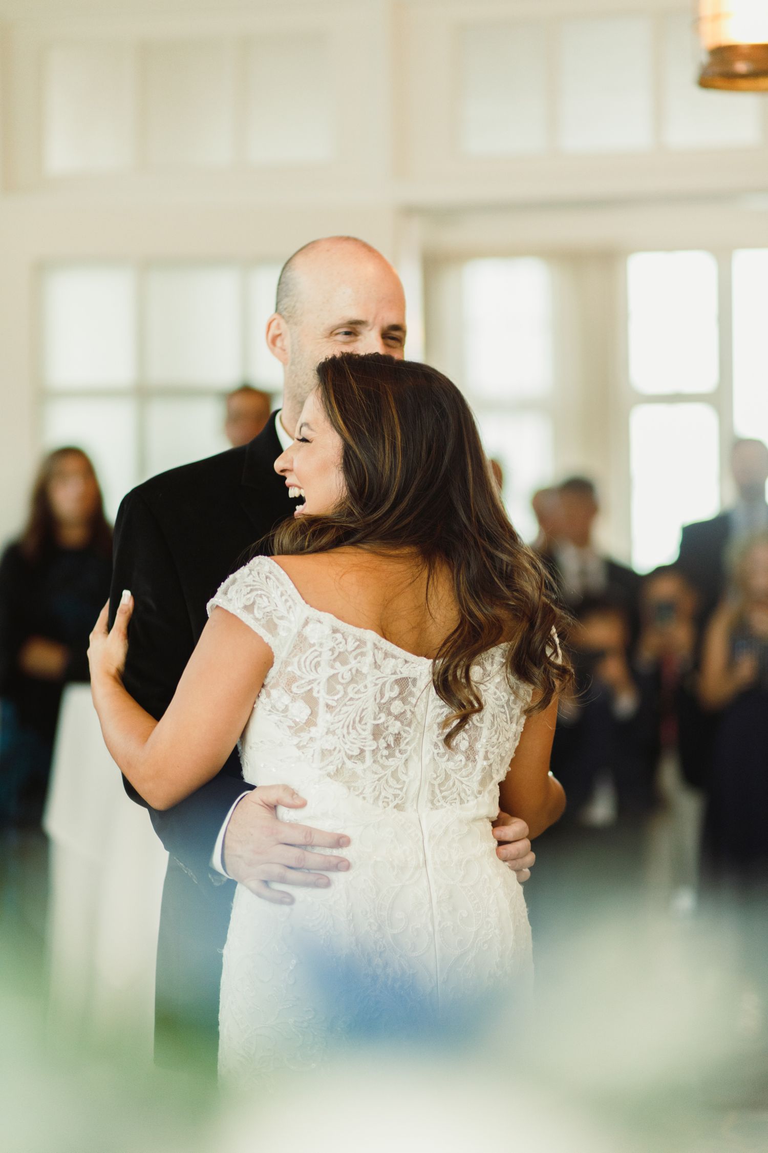 A couple shares an intimate dance moment during their wedding reception in a bright ballroom.