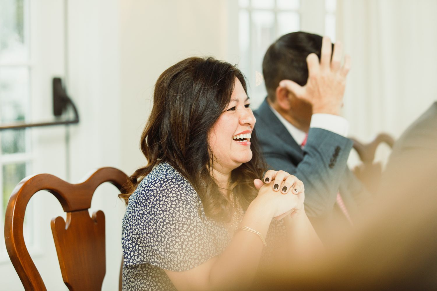 A person laughing heartily while seated at an elegant dining table.