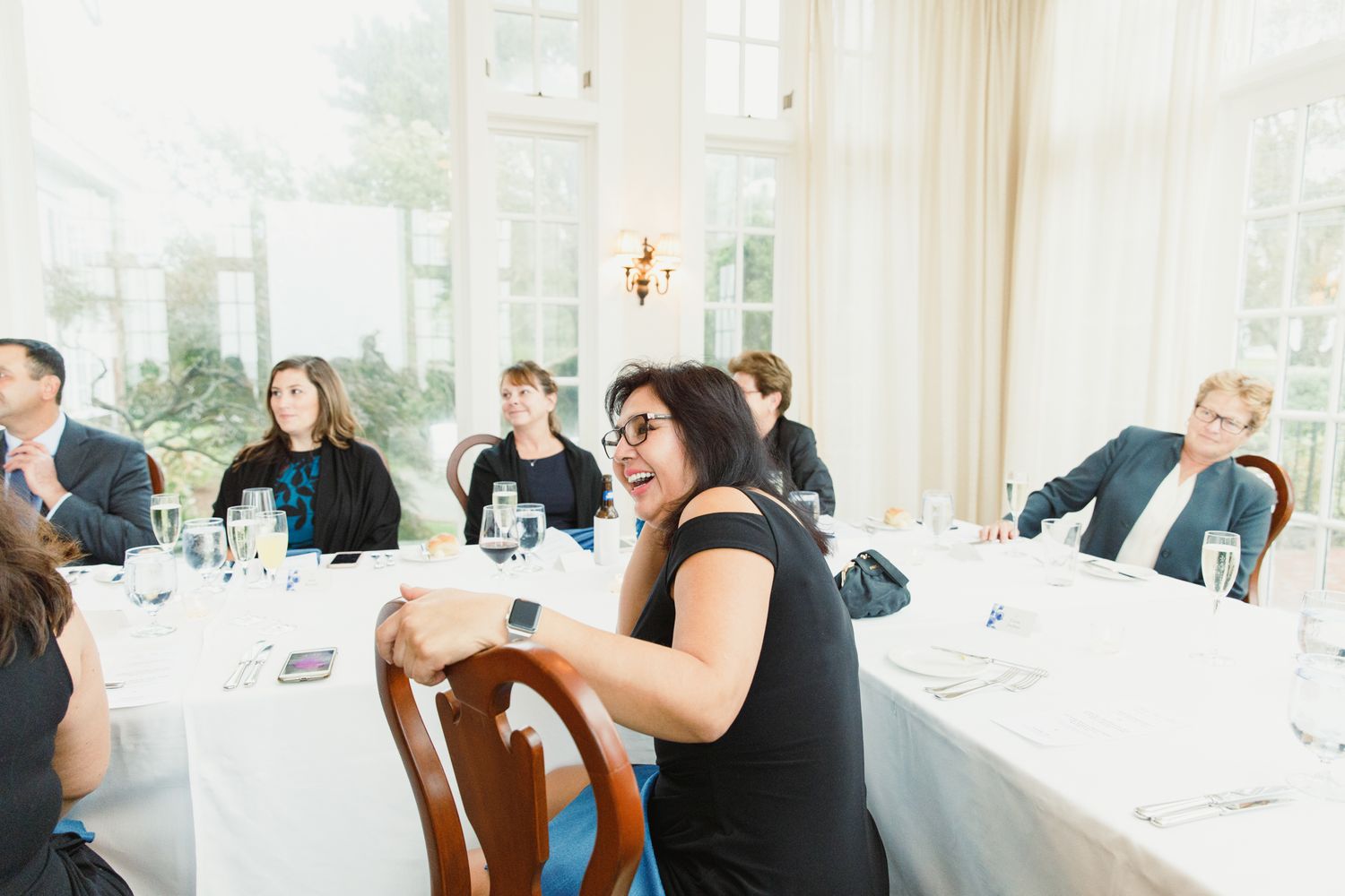 Wedding guests enjoy an elegant dinner reception in a bright room with large windows.