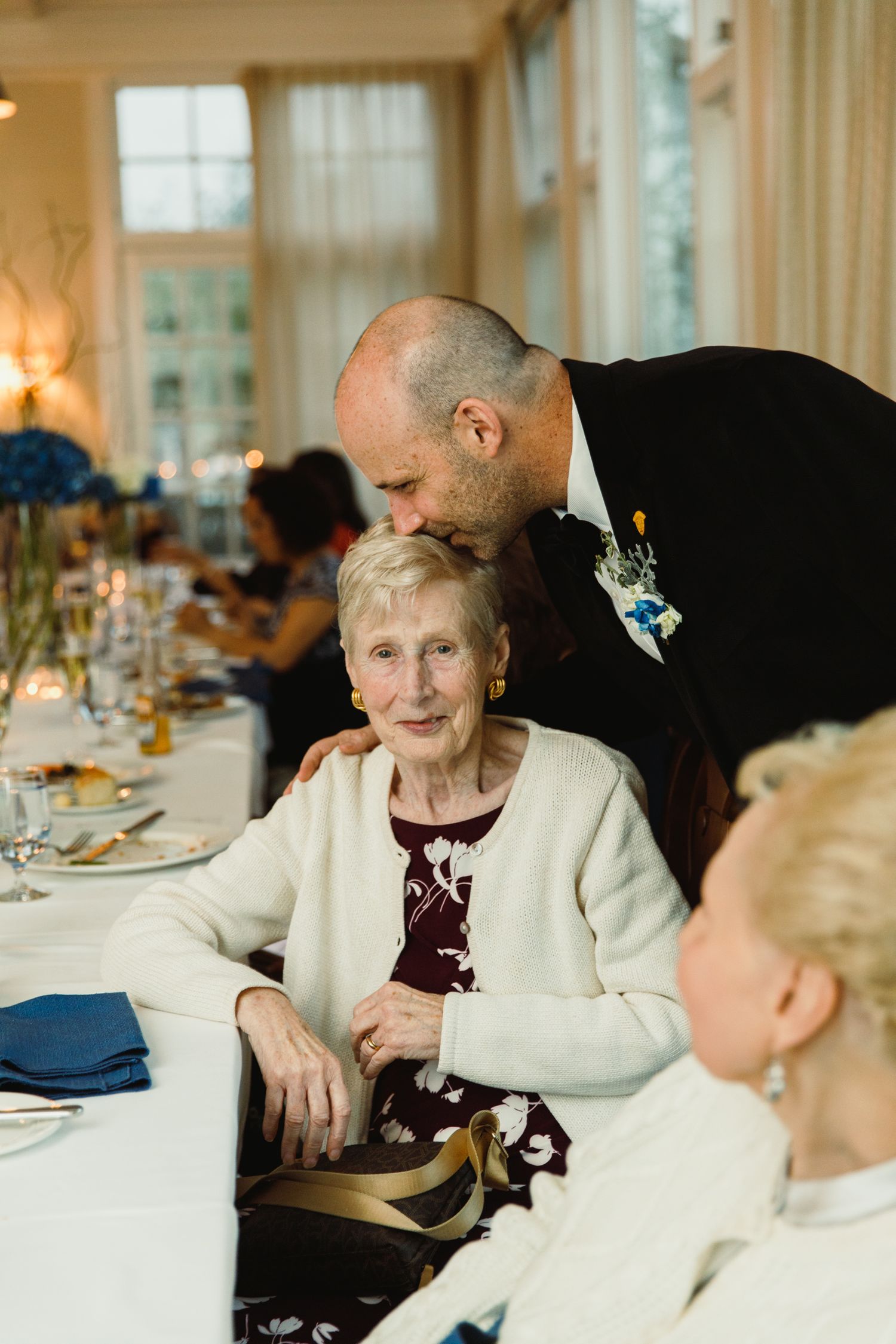Elderly woman in white sweater seated at elegant dining table during special event.
