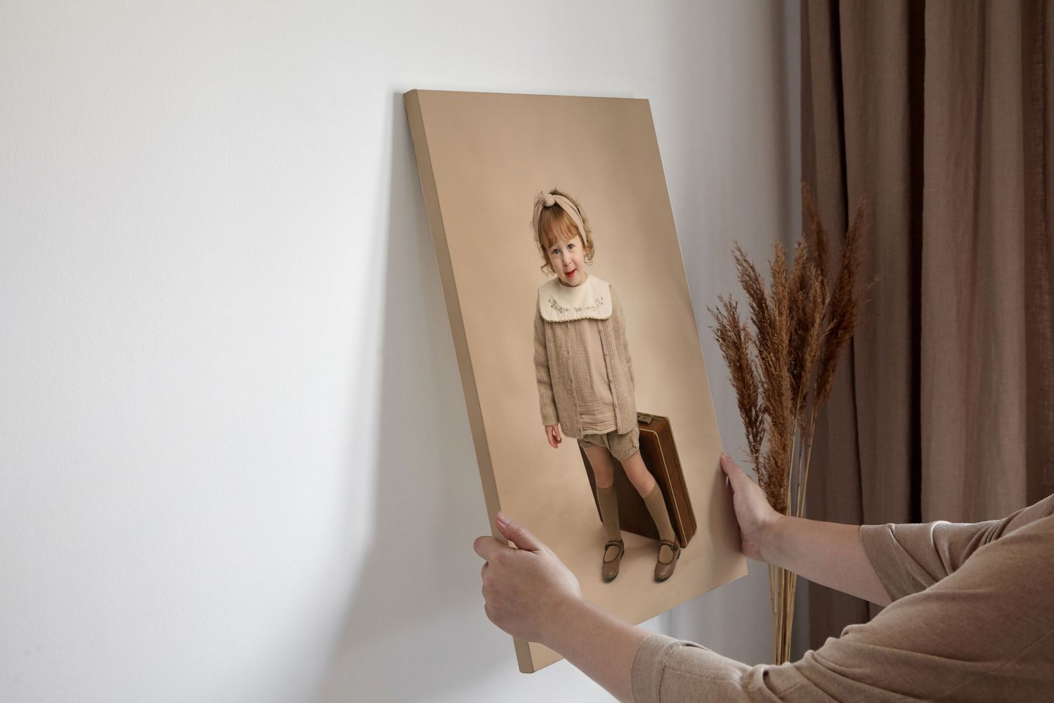 Hands displaying a sepia-toned portrait canvas against a neutral wall with dried pampas grass.