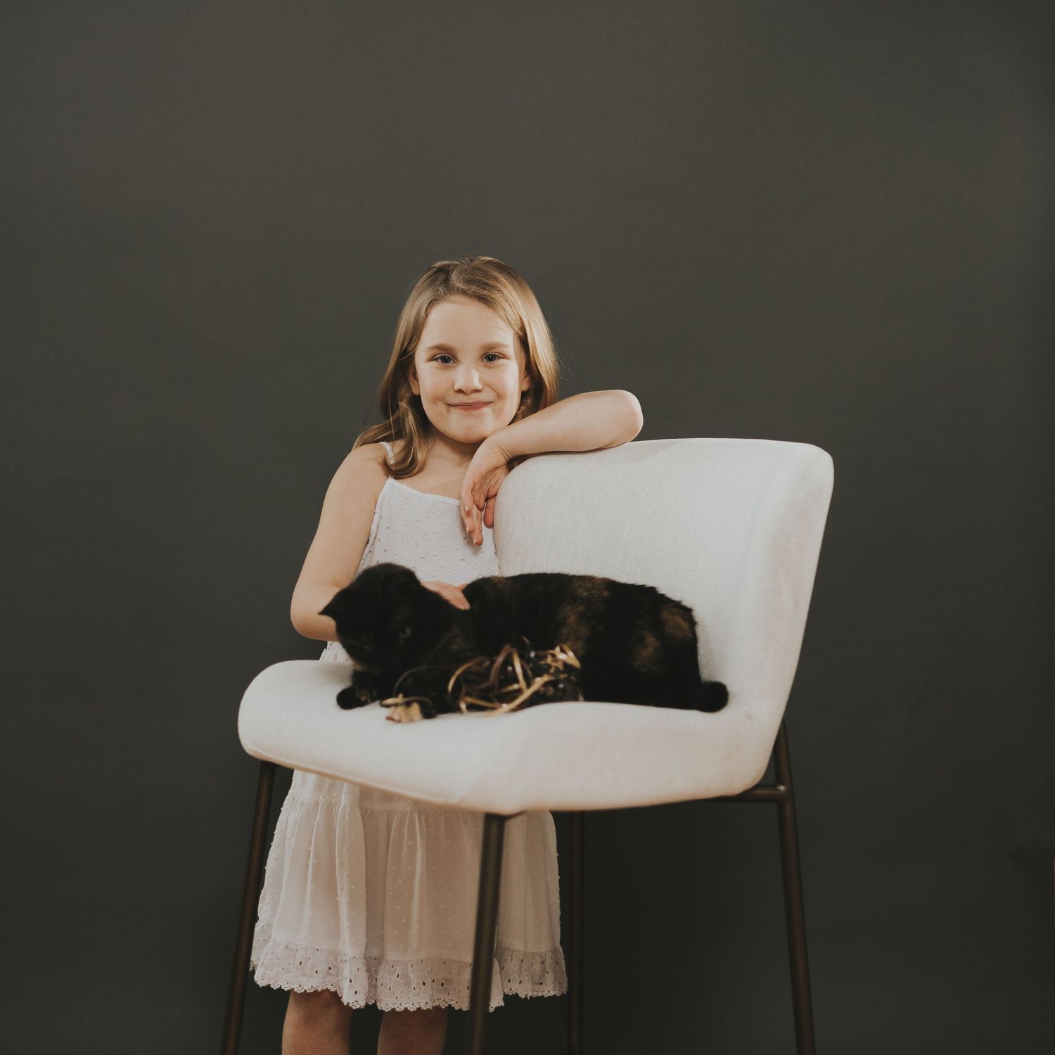 A black cat lounges on a white modern chair against a dark background.