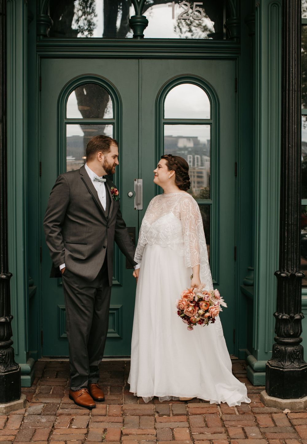 Bride and groom share a romantic moment before green double doors on their wedding day.