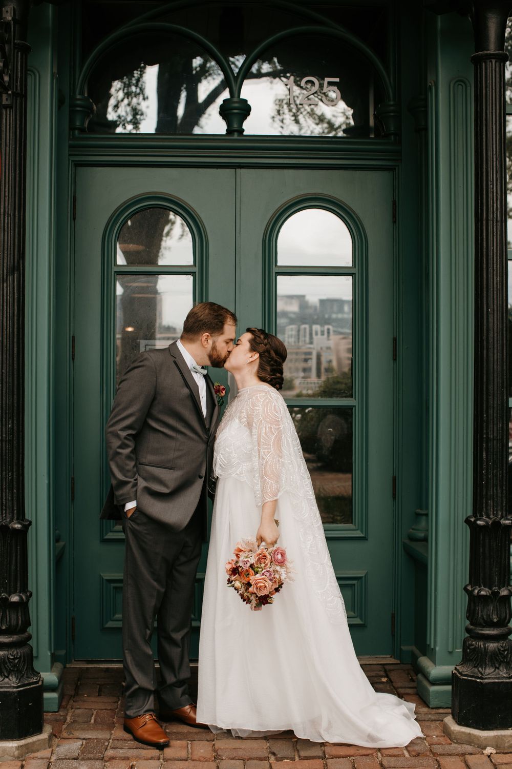 Bride and groom share a kiss in front of green arched doors on their wedding day.