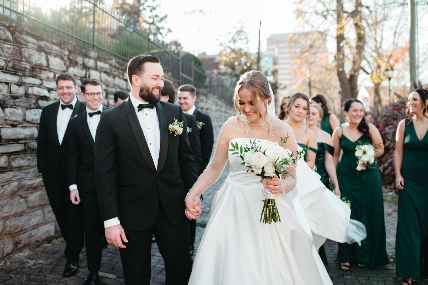 A wedding party poses together on stone steps with bridesmaids in elegant green dresses.