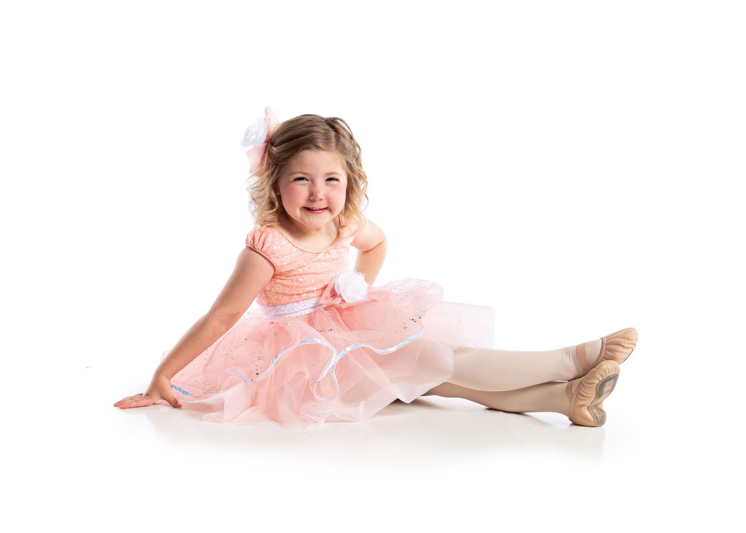 A young dancer in a pink tutu sitting on white backdrop