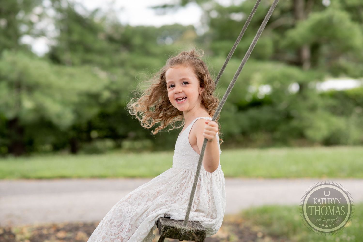 Girl in white dress swings joyfully outdoors with hair flowing in the wind.