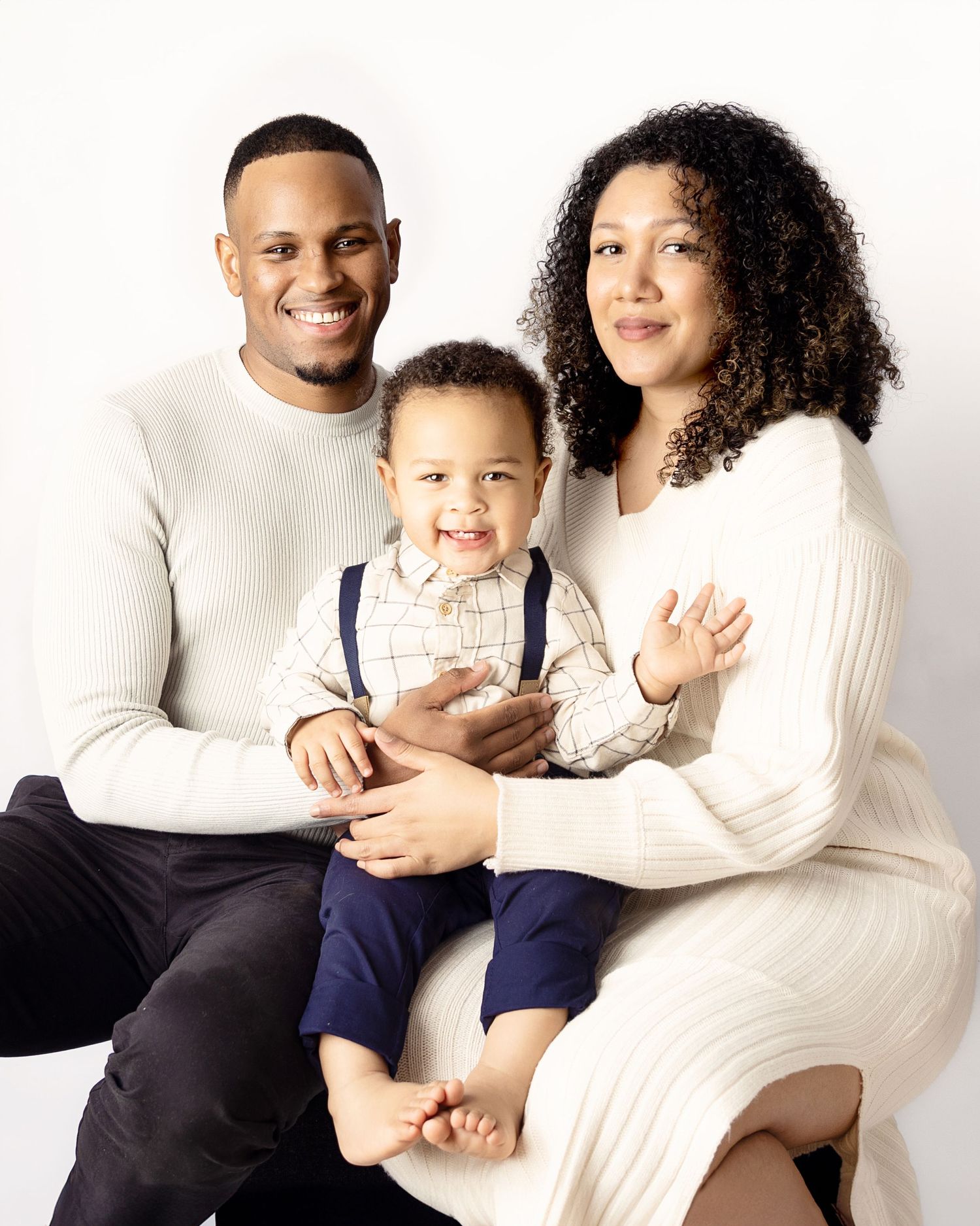 Portrait of a family in white sweaters sitting together against white background.