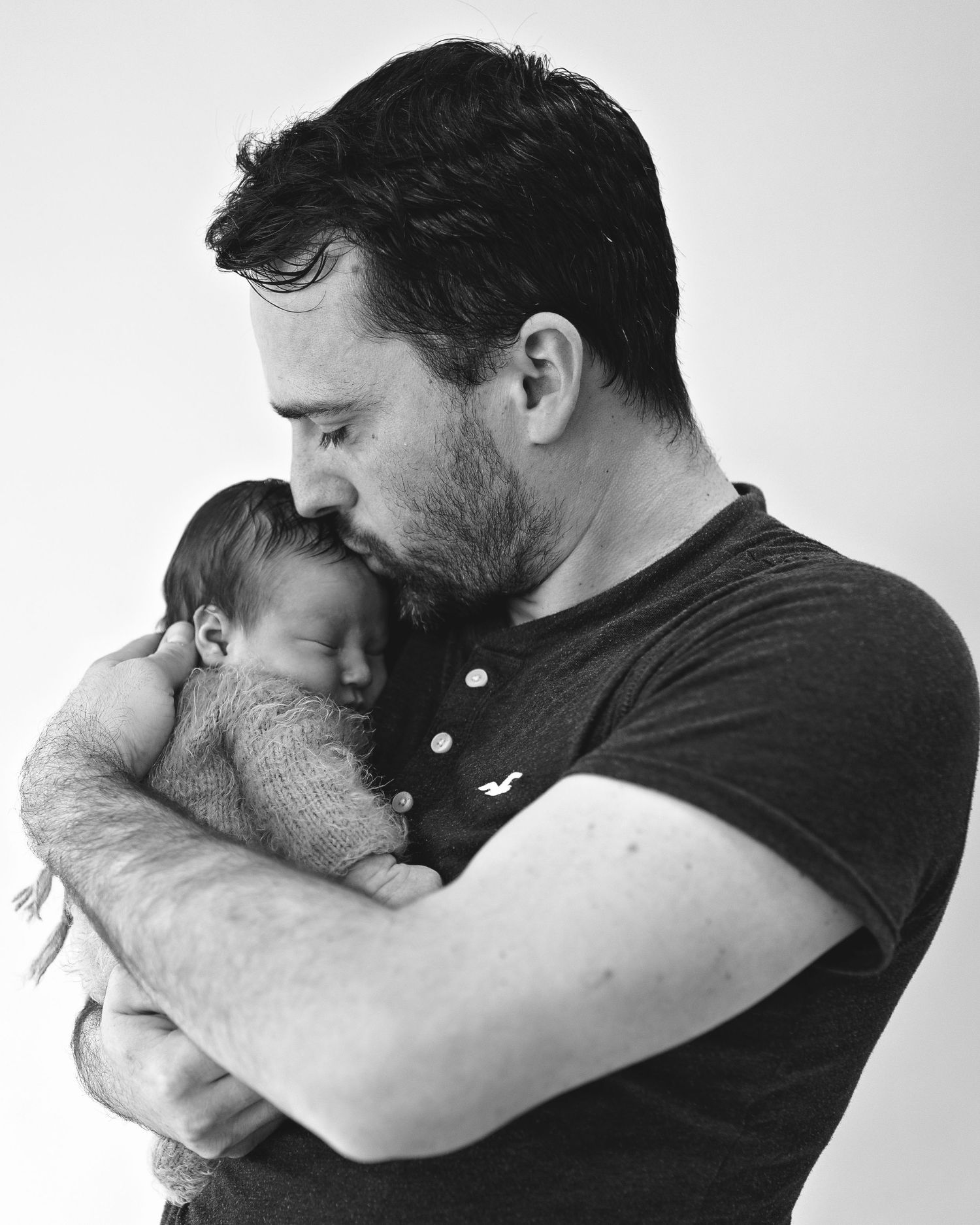 A tender black and white portrait of a father cradling his sleeping newborn against his chest.