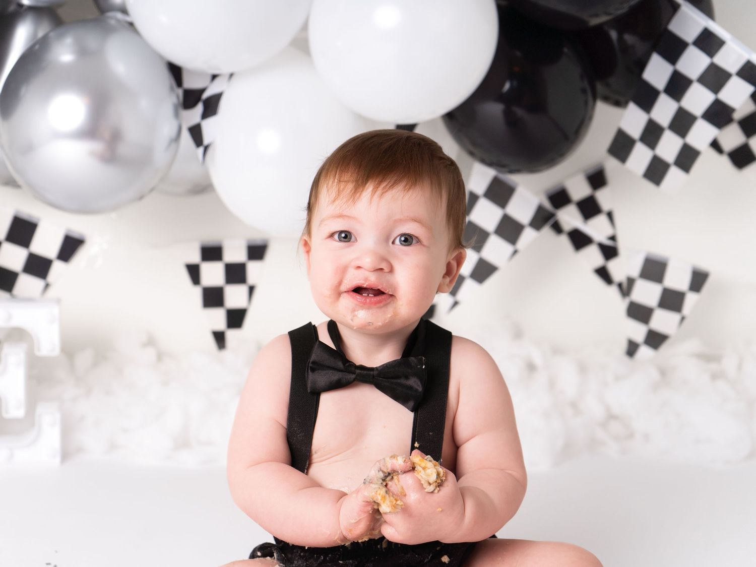 one year old boy holding cake smiling black and white first birthday with cake smash photographer in Doncaster.