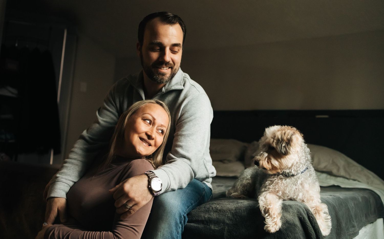 Smiling couple relaxing on bedroom floor with fluffy dog, in cozy home setting.